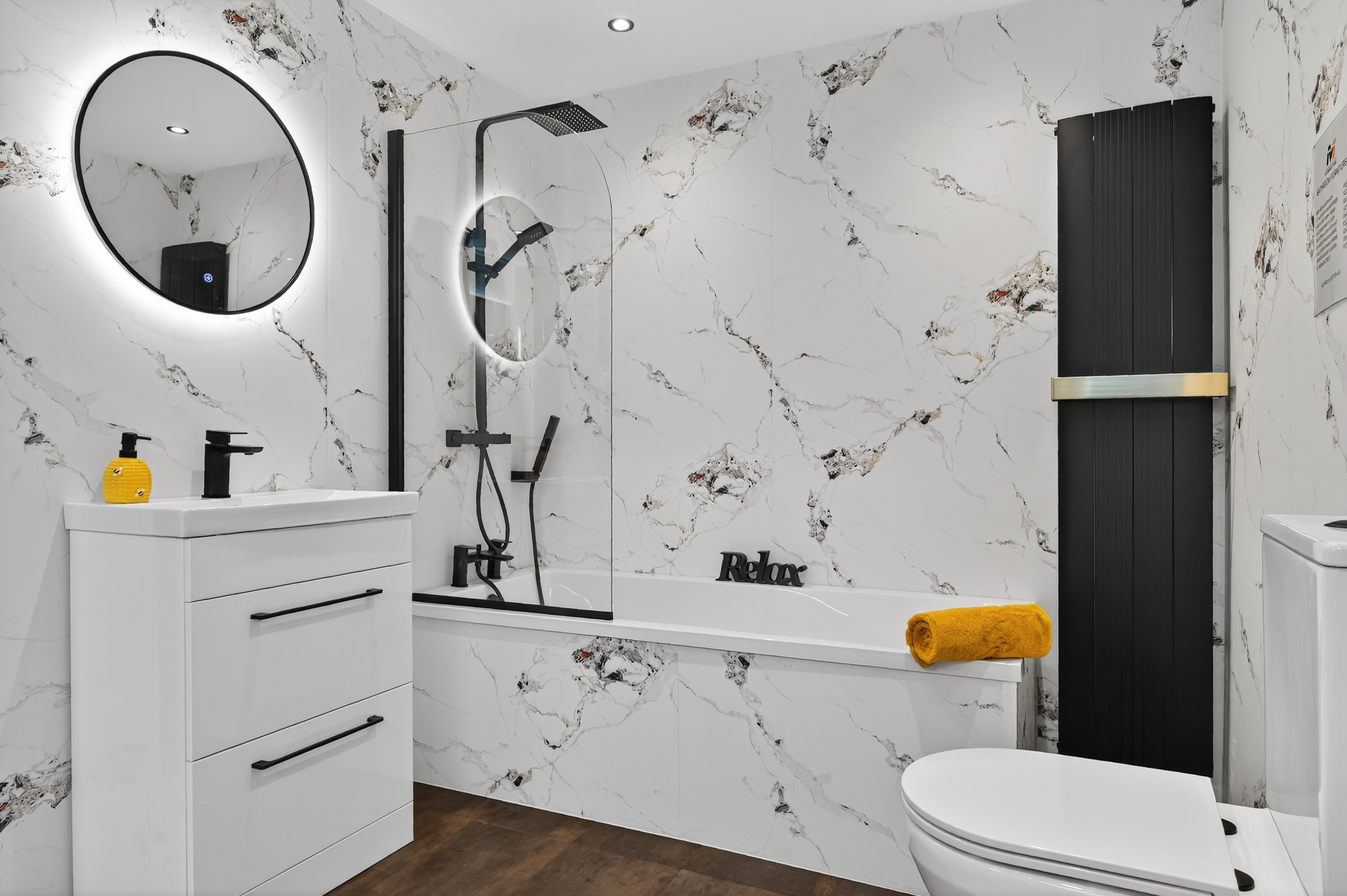 Bathroom display with white and black marble PVC wall panels matte black bath shower screen round LED mirror white gloss vanity and black vertical radiator in M1 Bathrooms Belfast showroom