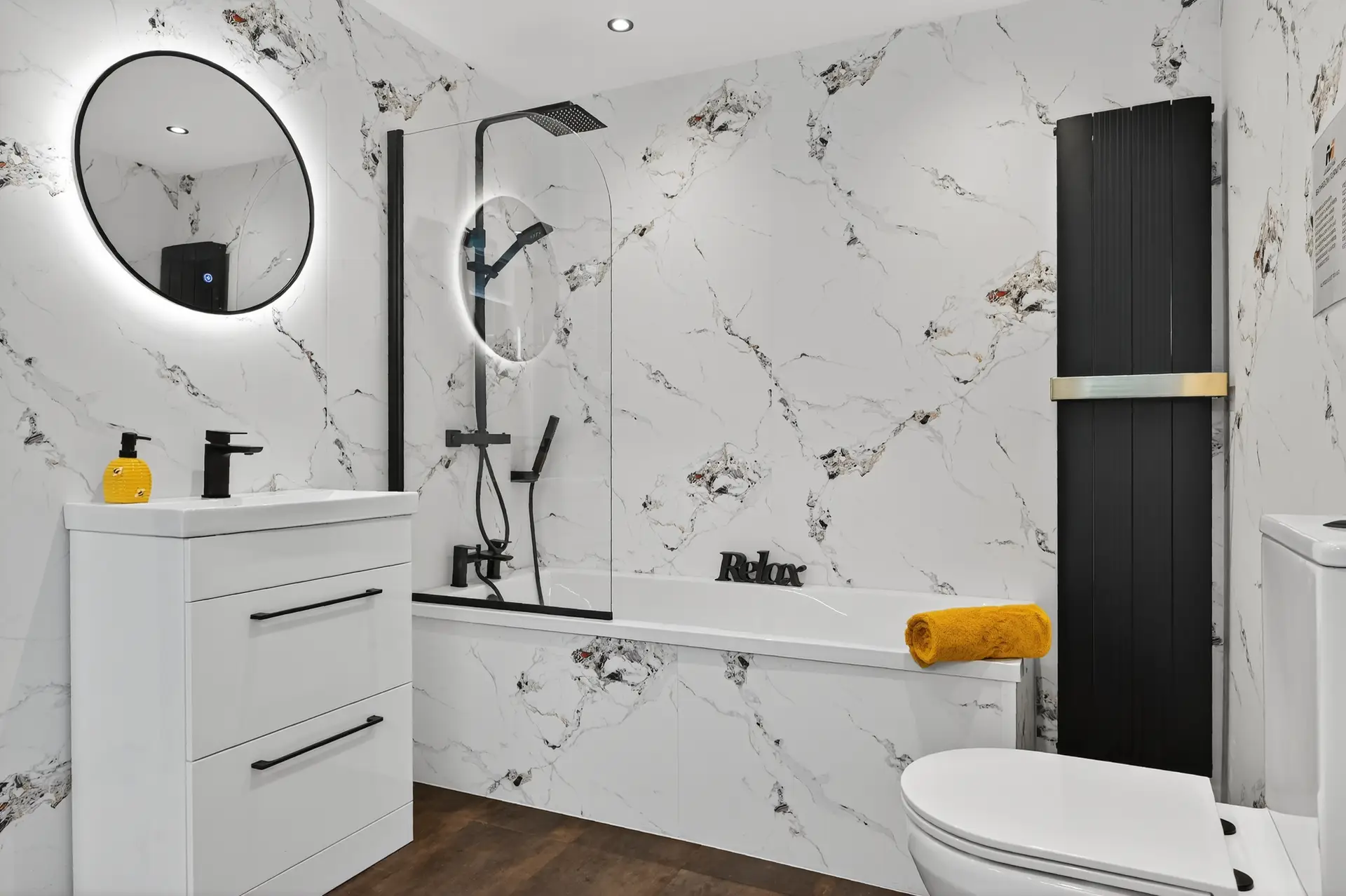 Bathroom display with white and black marble PVC wall panels matte black bath shower screen round LED mirror white gloss vanity and black vertical radiator in M1 Bathrooms Belfast showroom